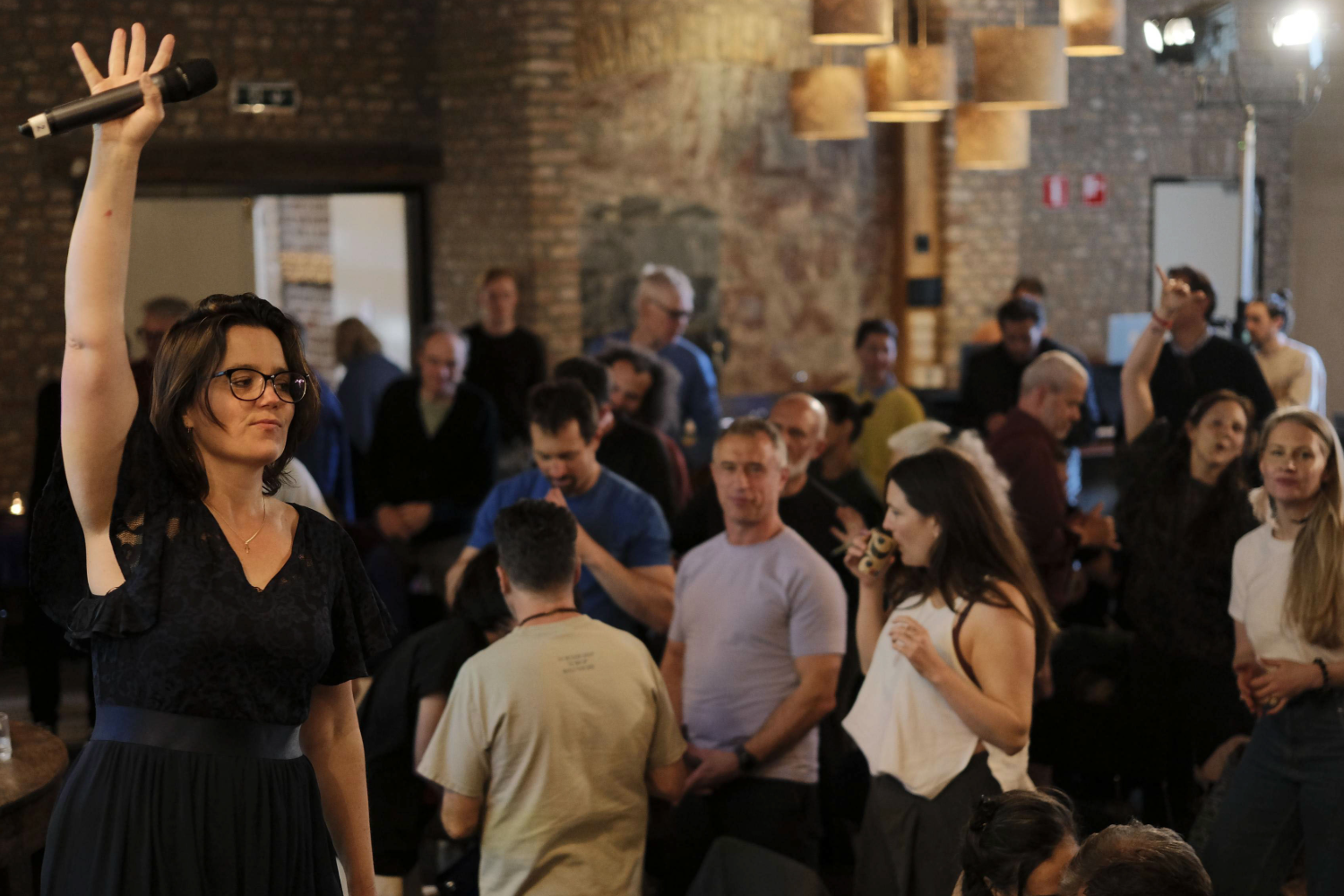 A woman raising a microphone high above a crowded room of participants